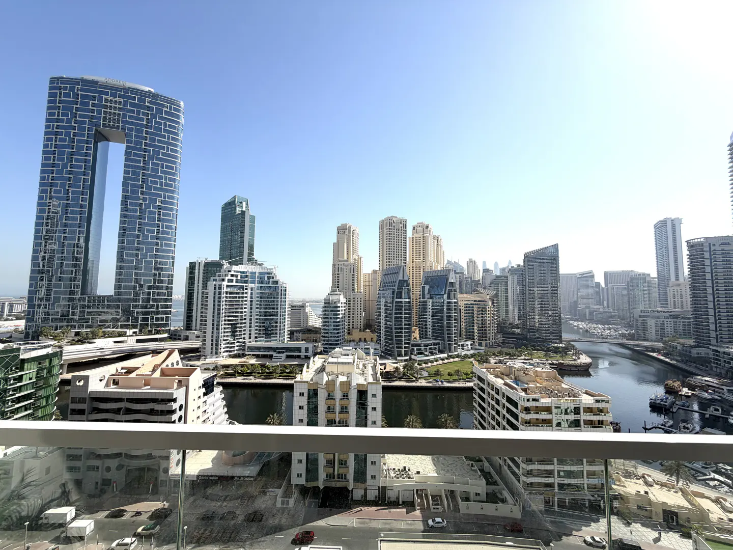 High-angle view of the Dubai Marina skyline with modern skyscrapers, a canal, and a clear blue sky from a balcony.