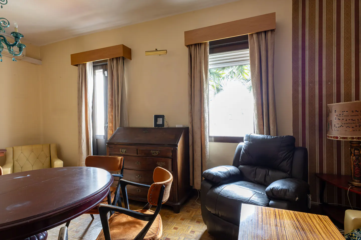 A living room with a dark wood table, brown leather chair, and a vintage desk near a window.