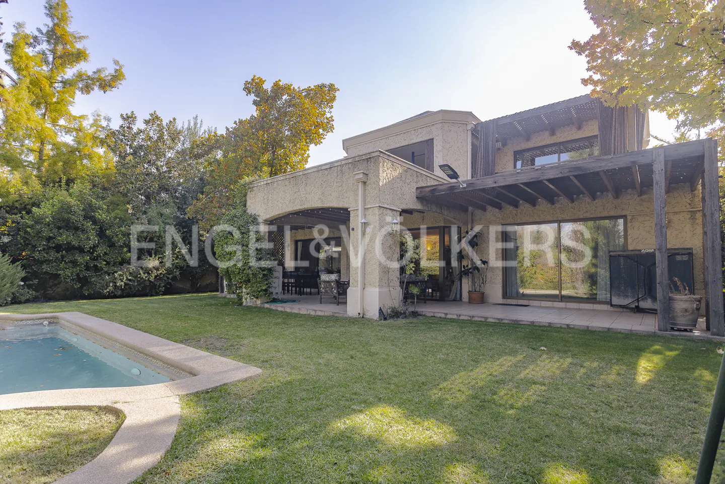Exterior view of a two-story house with a pool, patio, and green lawn. Trees surround the property.