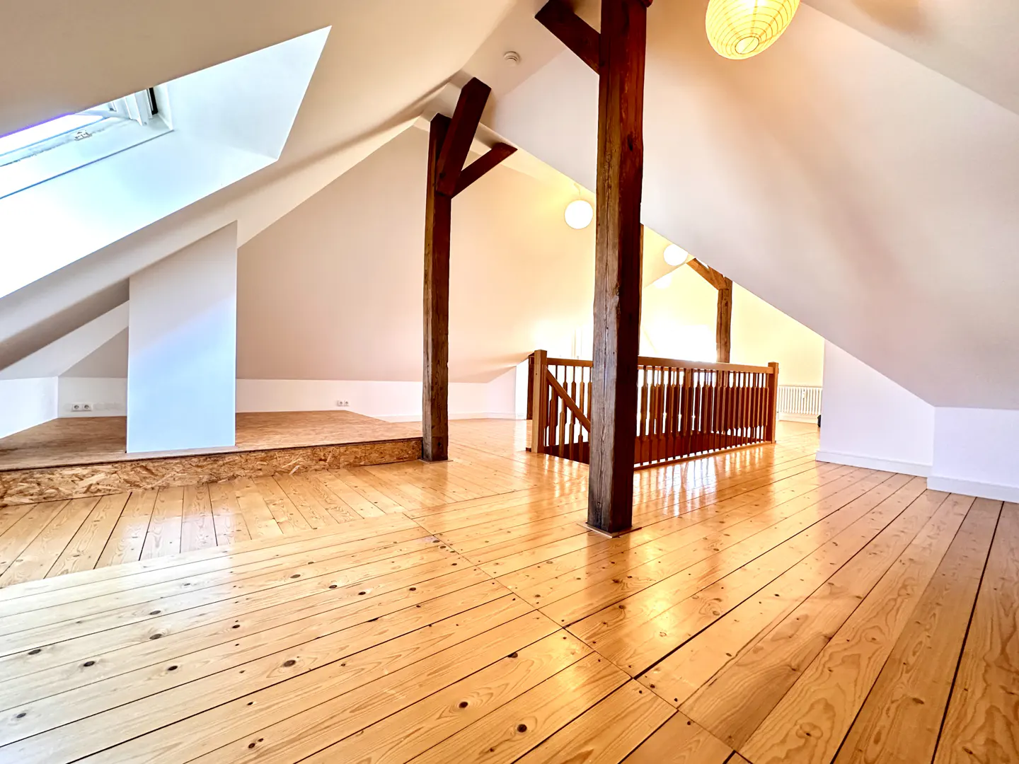 Attic room with wooden floors, white walls, and exposed beams. A skylight provides natural light. A wooden railing overlooks a lower level.