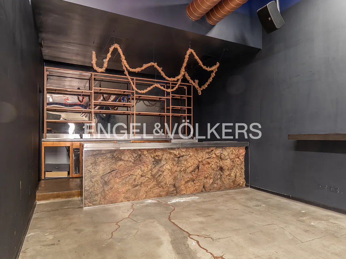Interior view of a commercial space with a bar, shelves, and dark gray walls. The bar has a textured brown front. Ropes hang from the ceiling.