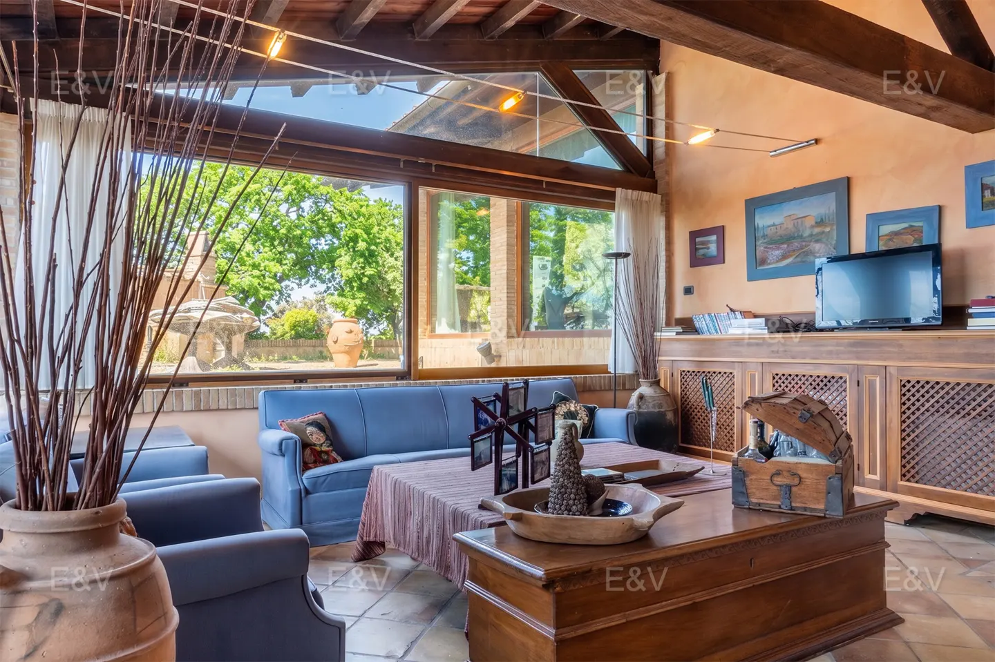 Living room with blue sofa and chairs, wooden coffee table, and large windows overlooking a green garden.