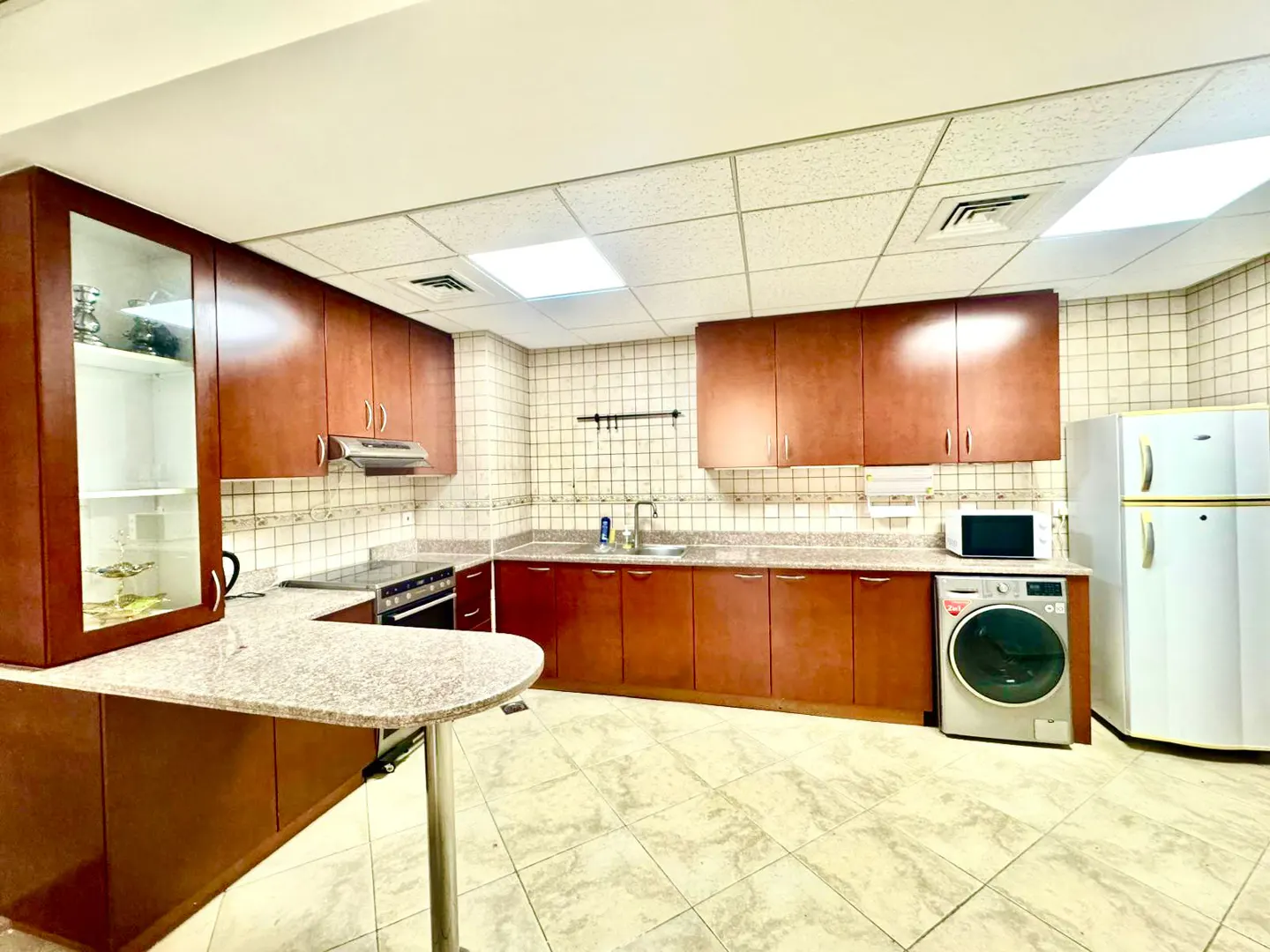 A well-lit kitchen with brown cabinets, a white refrigerator, and a breakfast bar with a granite countertop.