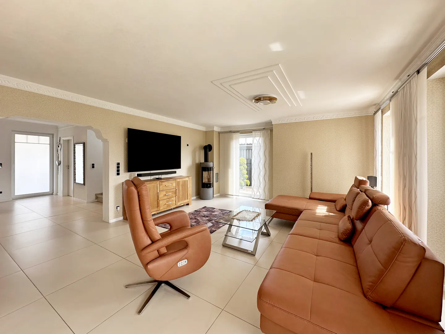 Bright living room with tan walls, white tile floor, and brown leather furniture. A TV, wood cabinet, and fireplace are against the wall.