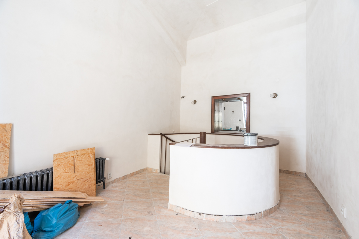 An empty room under renovation with white walls, tiled floors, a curved staircase railing, and construction materials. [AI-generated text]