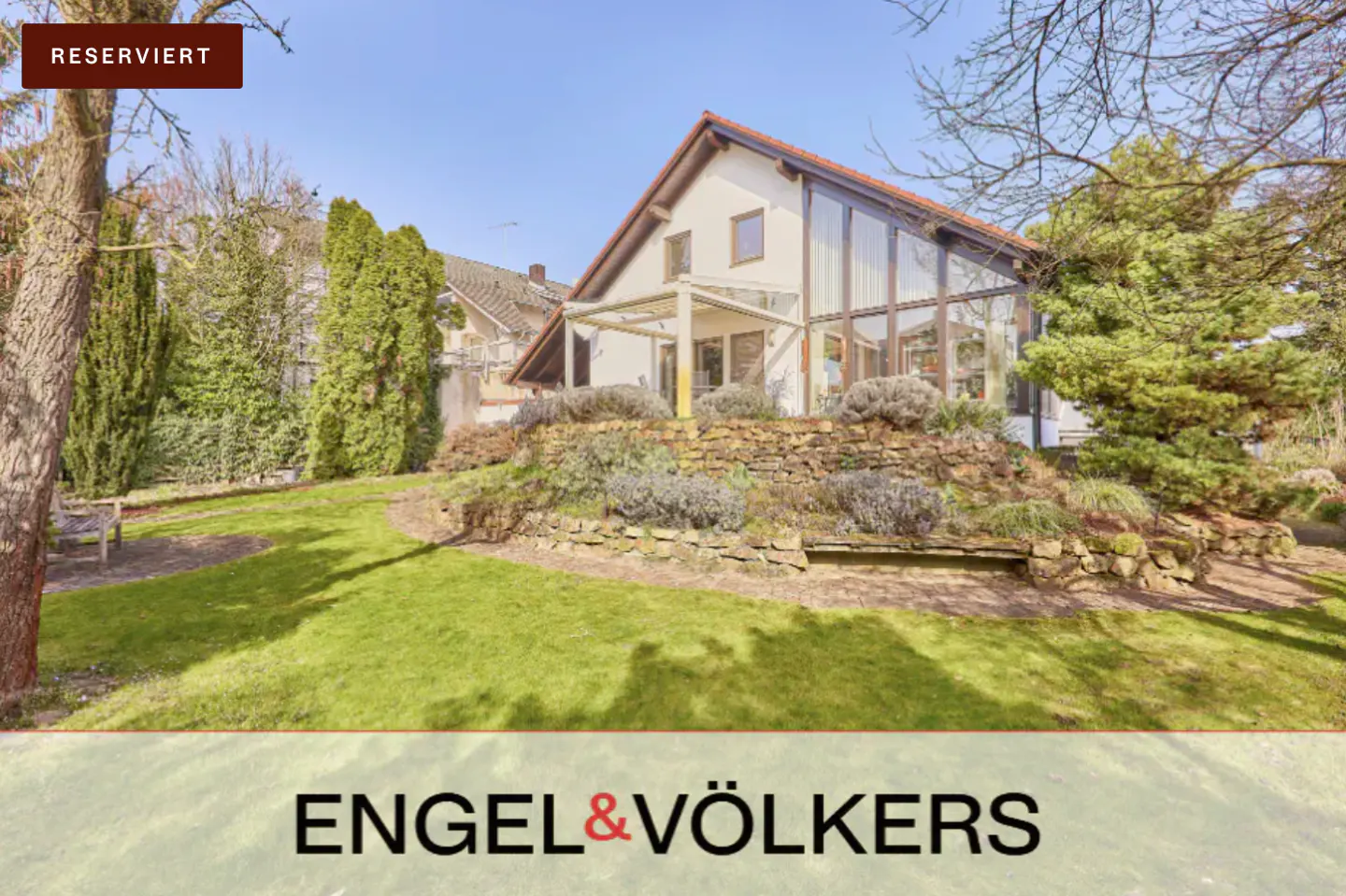 Modern house with large windows and a stone garden terrace, set in a green yard under a clear blue sky. Reserved status.