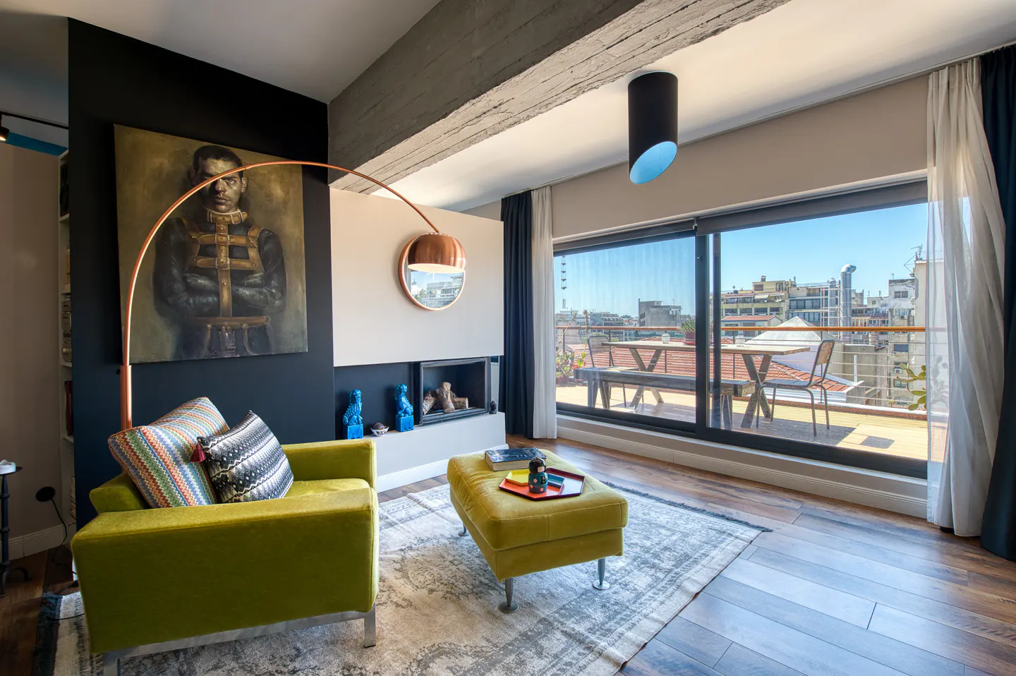 Living room with a green chair, ottoman, and a painting on a black wall. A fireplace and balcony with city views are visible.