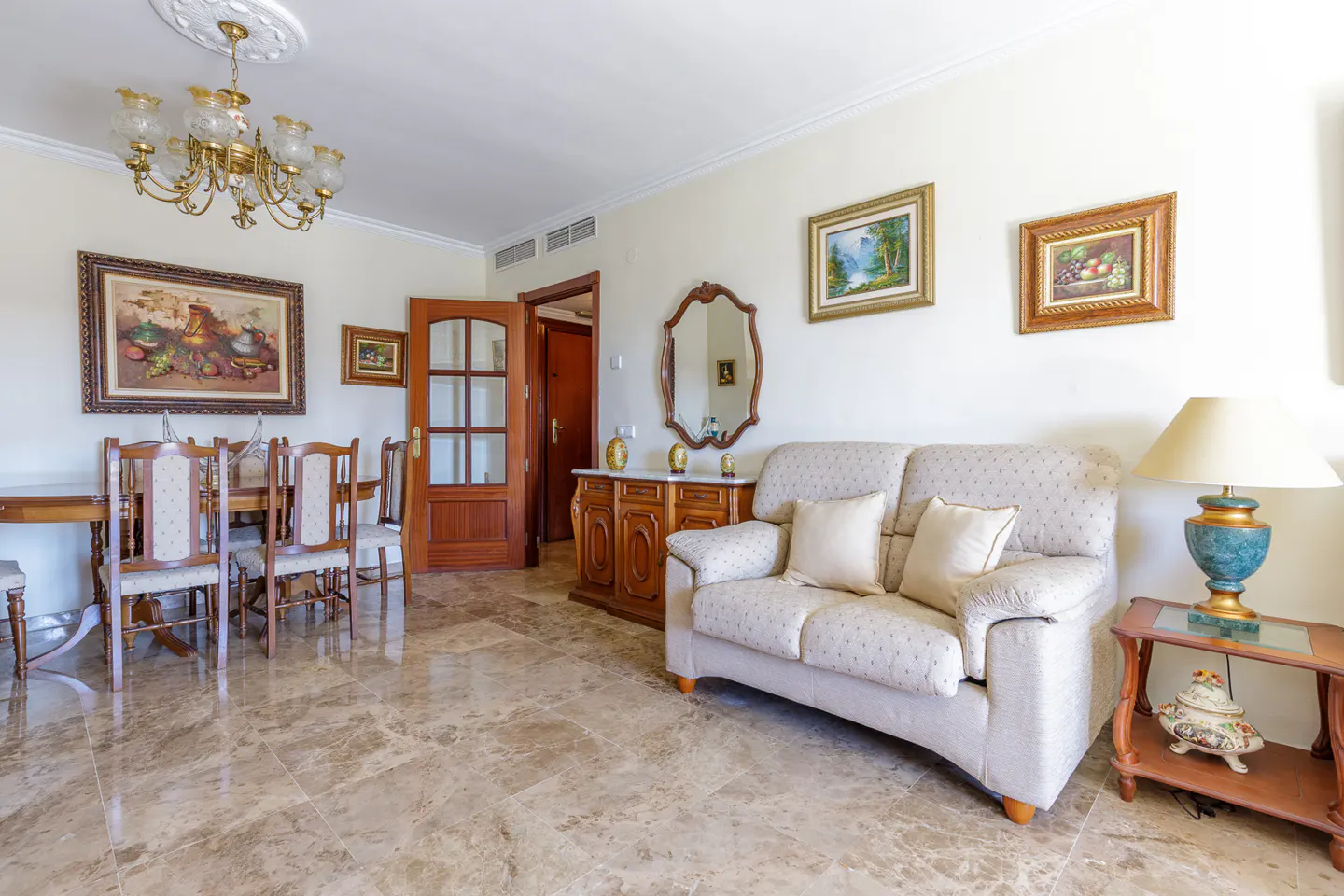 A living room with a dining table, a sofa, and a wooden cabinet on a marble floor.