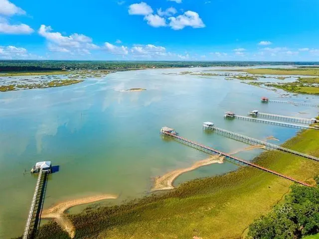 Aerial view of a wide river with docks extending from the grassy shoreline under a blue sky with scattered clouds.