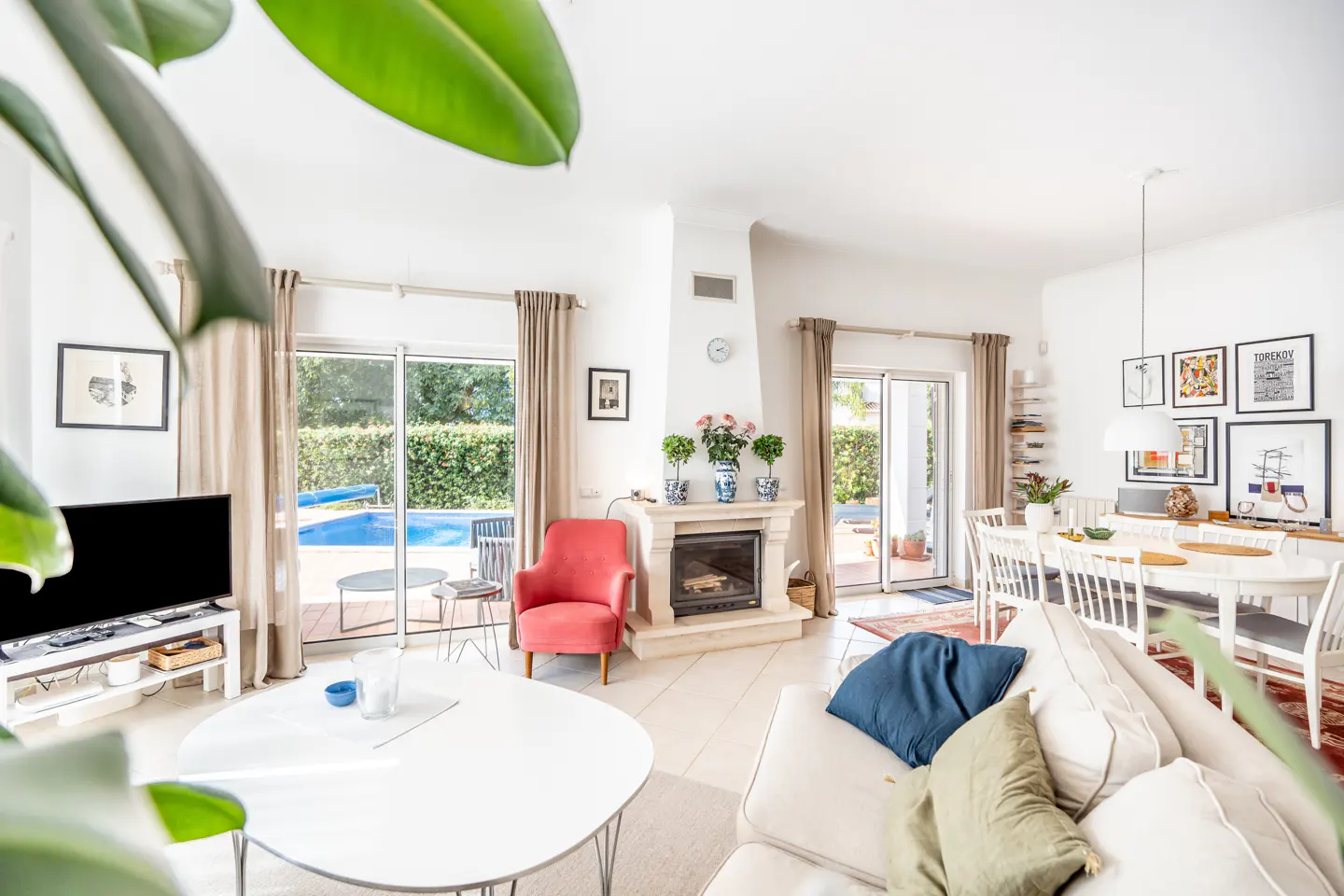 Bright living room with white walls, a fireplace, and a view of a pool through sliding glass doors. A white sofa and table are in the foreground.