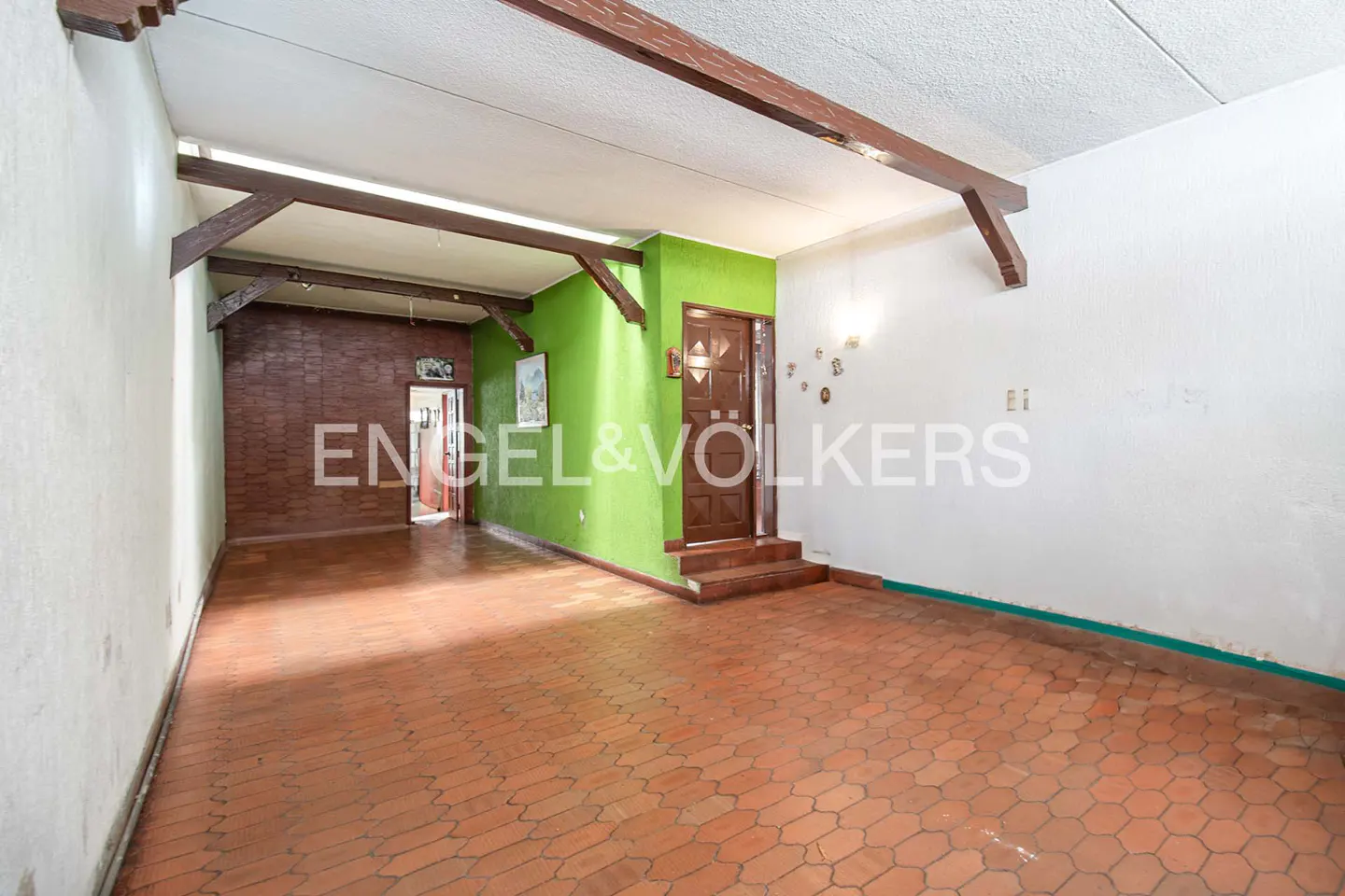 A living room with brown tile floors, white and green walls, and exposed wooden beams.