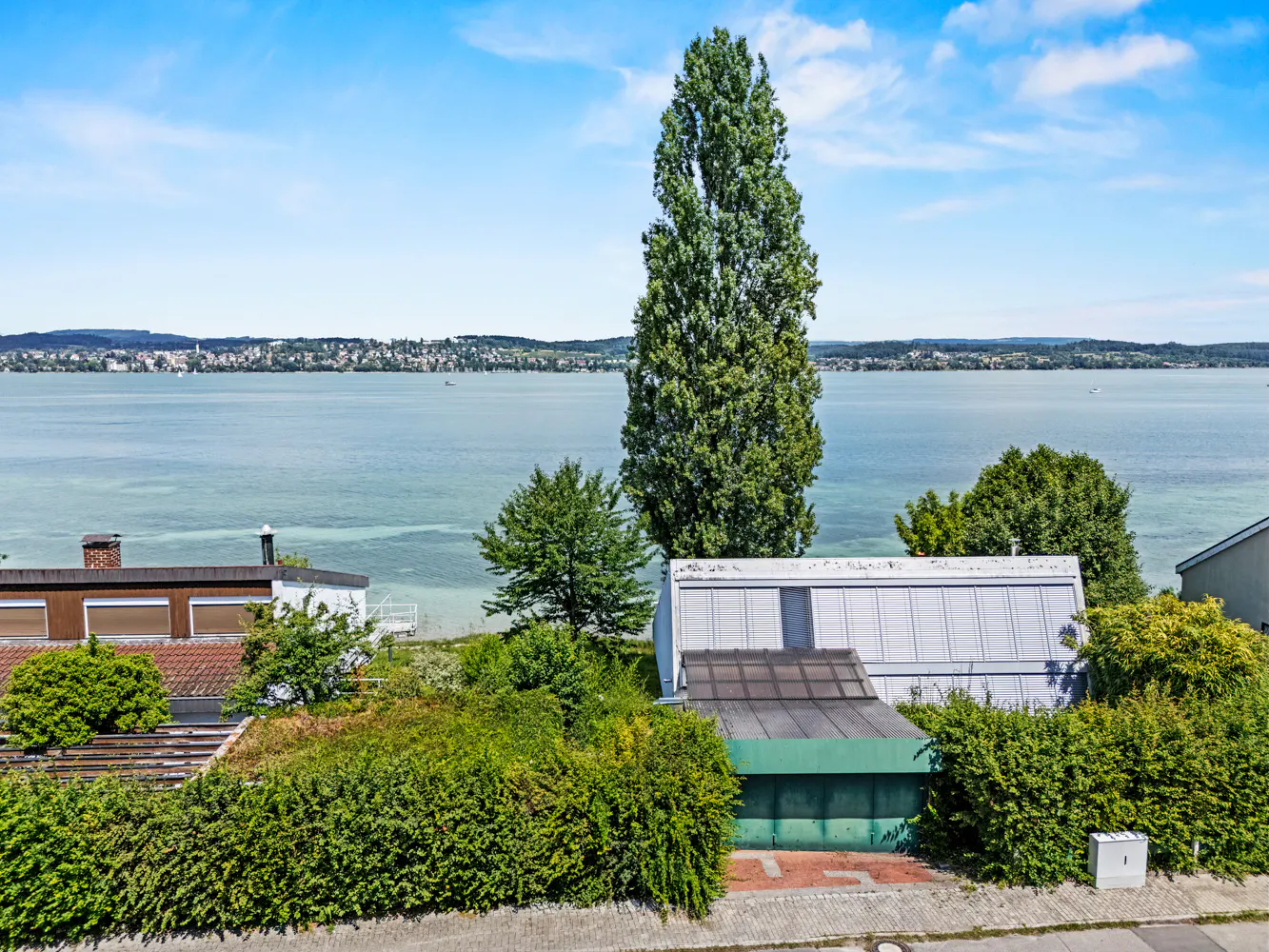 View of houses with green bushes and a lake in the background under a blue sky.