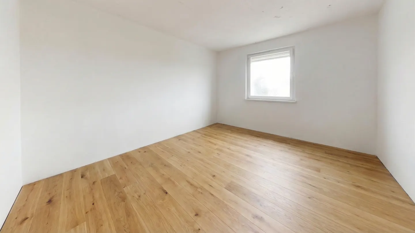 Bright, empty room with light wood floors, white walls, and a window with white trim.
