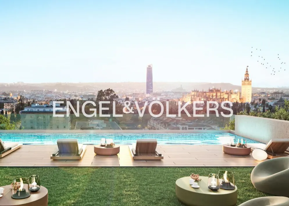 Rooftop terrace with an infinity pool, lounge chairs, and a panoramic view of the Seville city skyline at sunset.