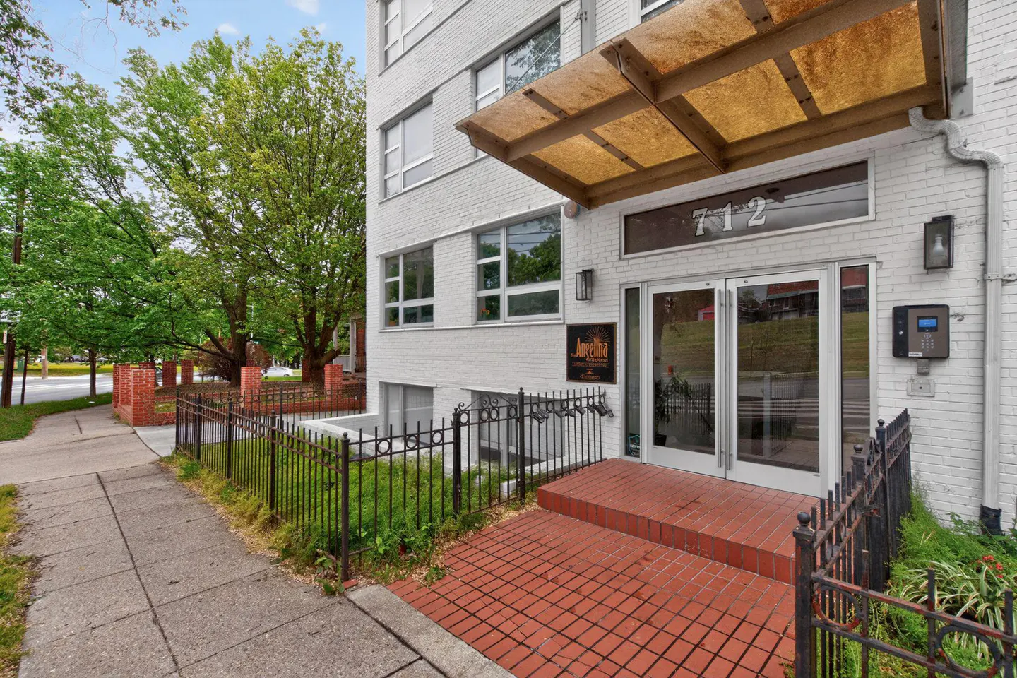 Exterior view of a white brick apartment building with a red brick entrance and awning. Address number 712 is above the glass doors.