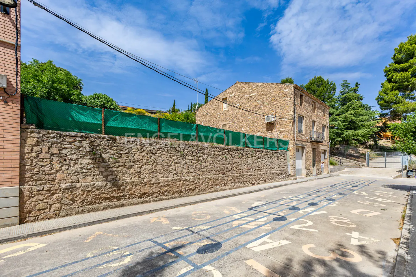 Exterior view of a stone house with a stone wall and a green fence, with musical notes painted on the street.