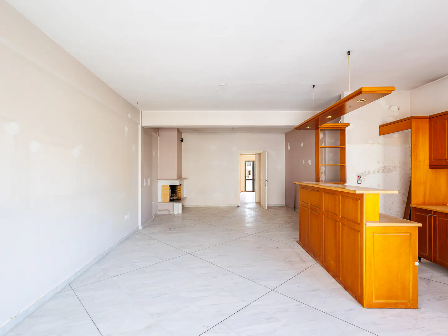 Spacious room under renovation with light tile floors, a wooden bar counter, and a fireplace in the background.