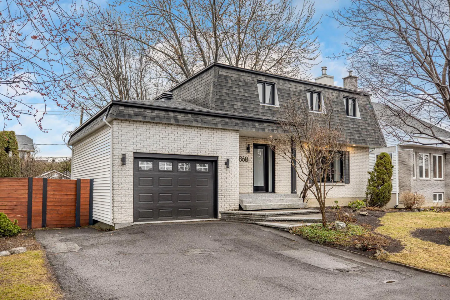 Exterior view of a two-story house with white brick, a dark gray roof, and a black garage door.