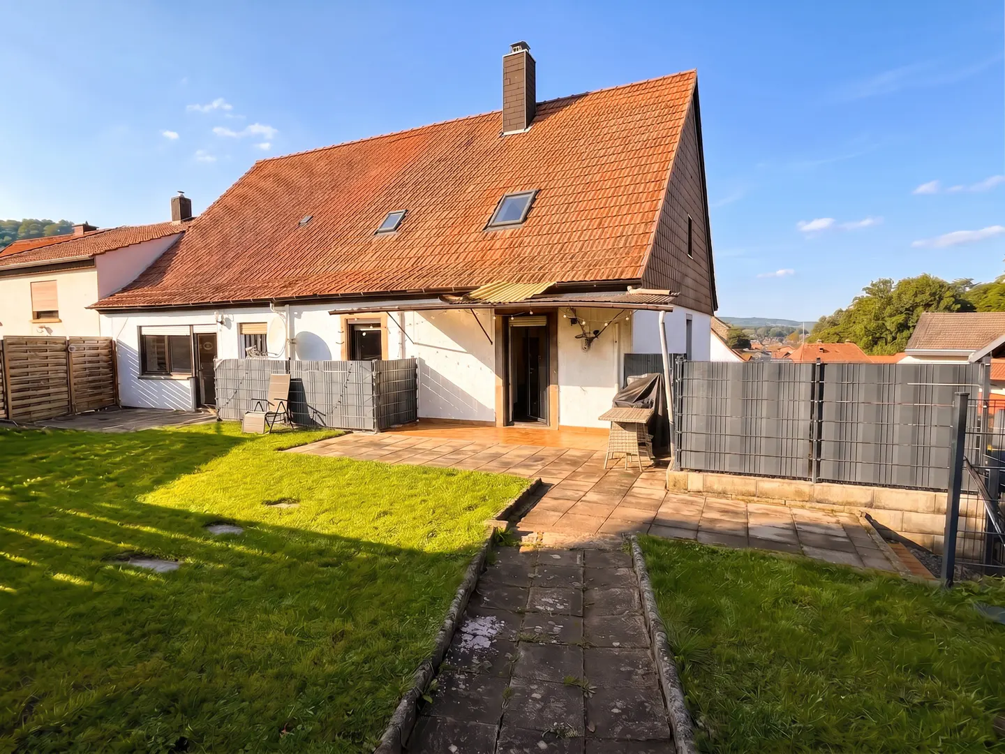A white house with a red tile roof, a green lawn, and a stone walkway under a blue sky.