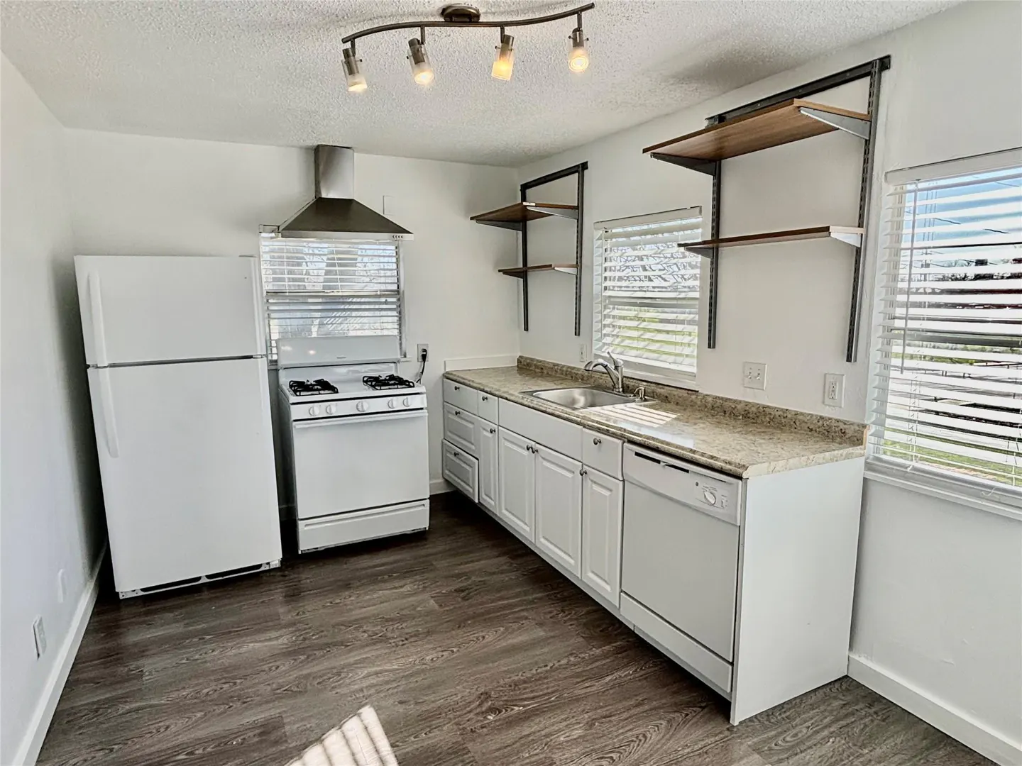 Bright kitchen with white appliances, cabinets, and walls. Dark wood-look floors and open shelving. Natural light from window.