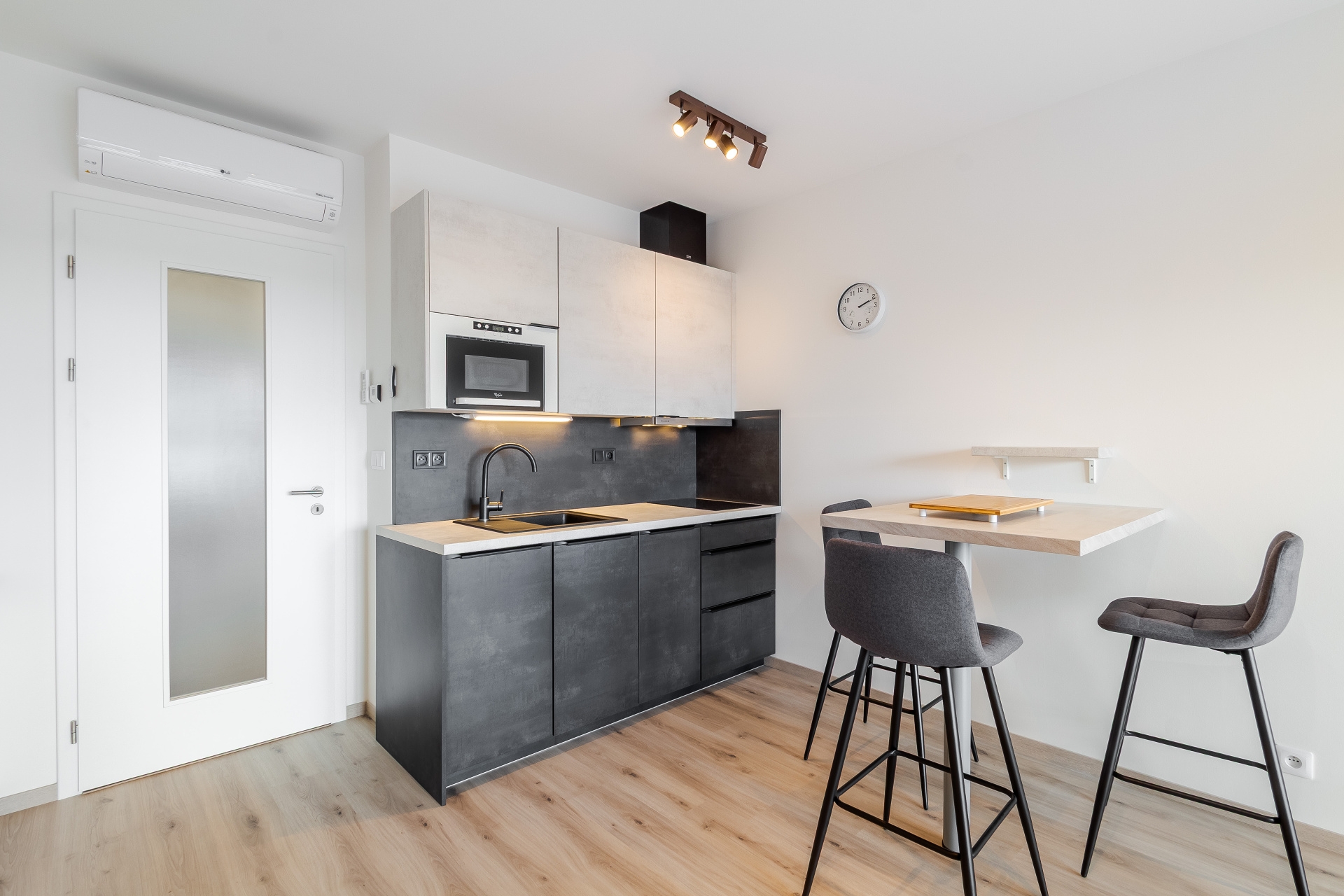 Modern kitchen with dark grey lower cabinets, white upper cabinets, a breakfast bar with two stools, and light wood floors. [AI-generated text]