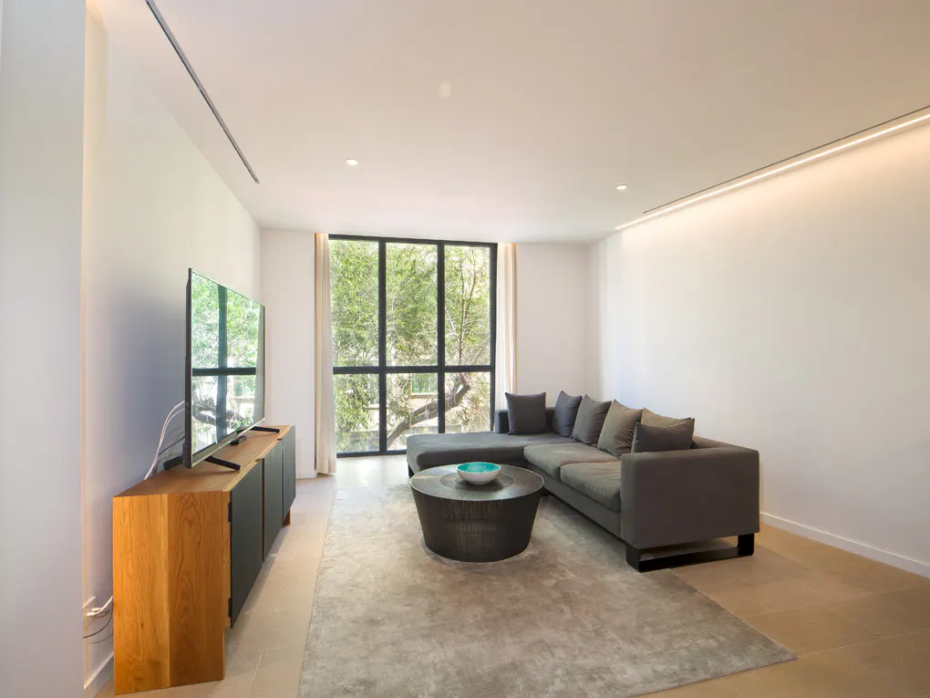 Living room with gray sectional sofa, round coffee table, TV on wood cabinet, and large window with trees outside.
