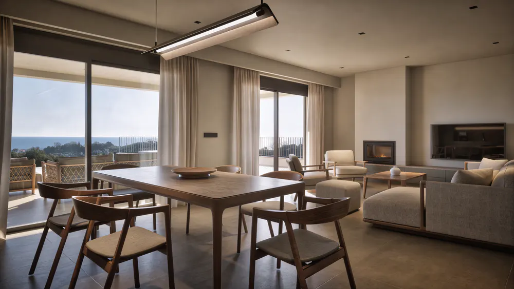 Modern open-plan living room with wooden dining set, beige sofa, fireplace, and floor-to-ceiling windows overlooking the sea.
