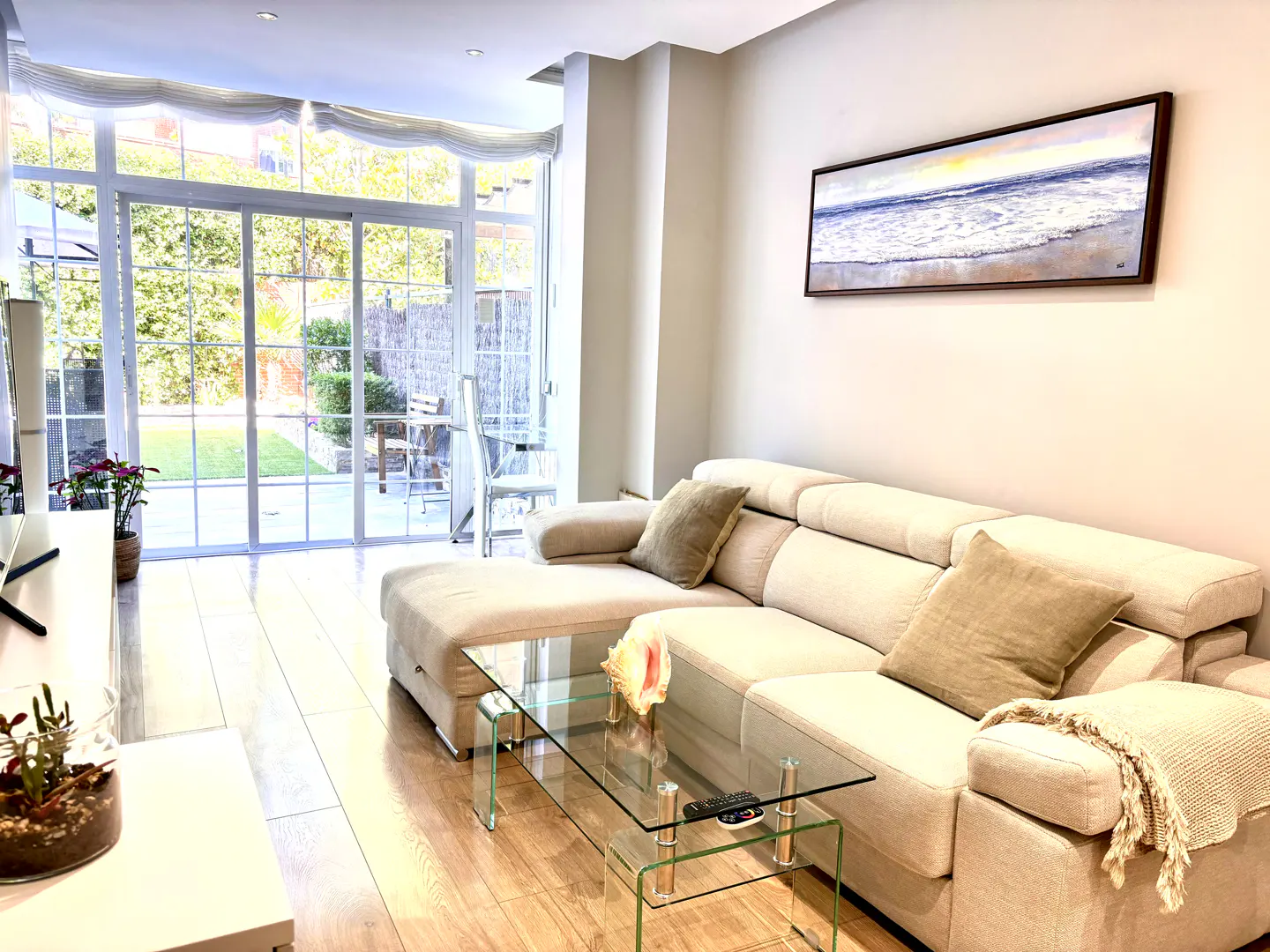 Bright living room with a beige sectional sofa, glass coffee table, and large sliding doors opening to a garden patio.