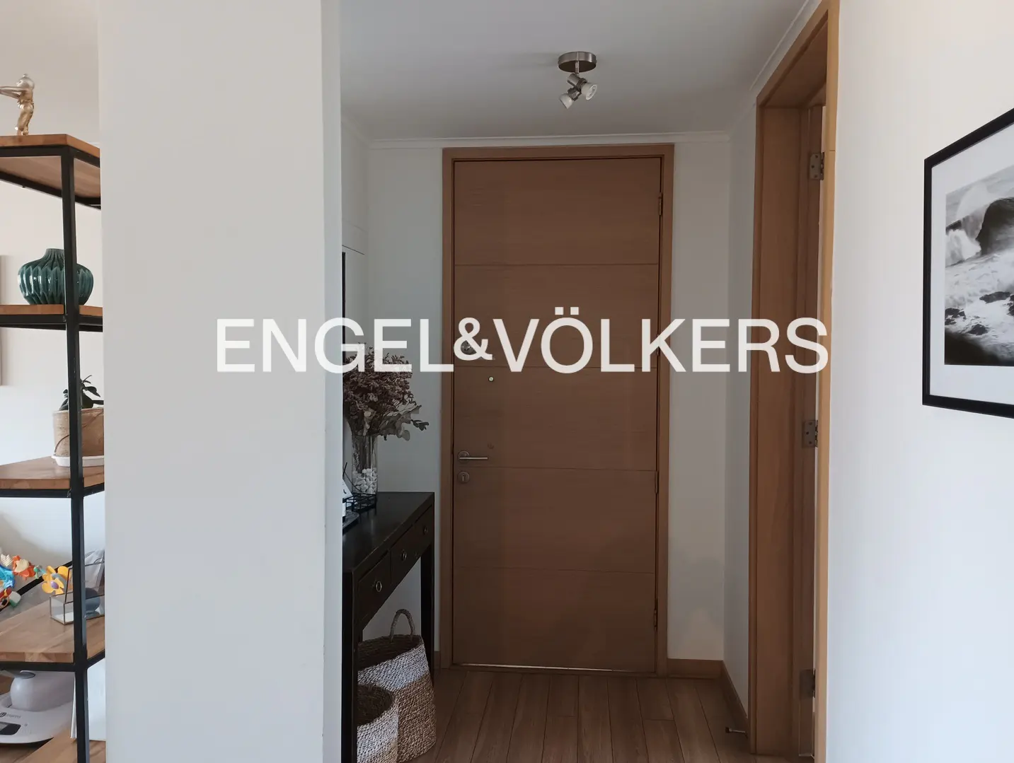 A bright entryway with a wooden front door, console table, and a black-framed print on a white wall.