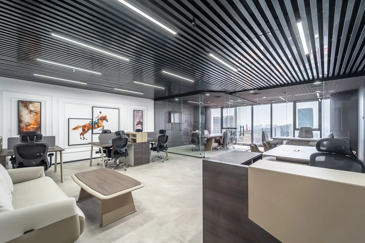 Modern office space with desks, chairs, and a glass-walled conference room. Artwork adorns the walls, and large windows offer a city view.