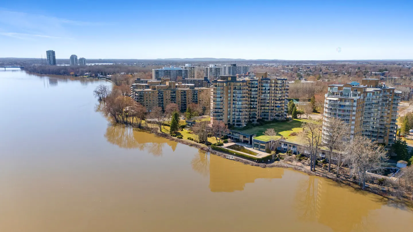 Aerial view of tan apartment buildings along a riverbank under a blue sky.