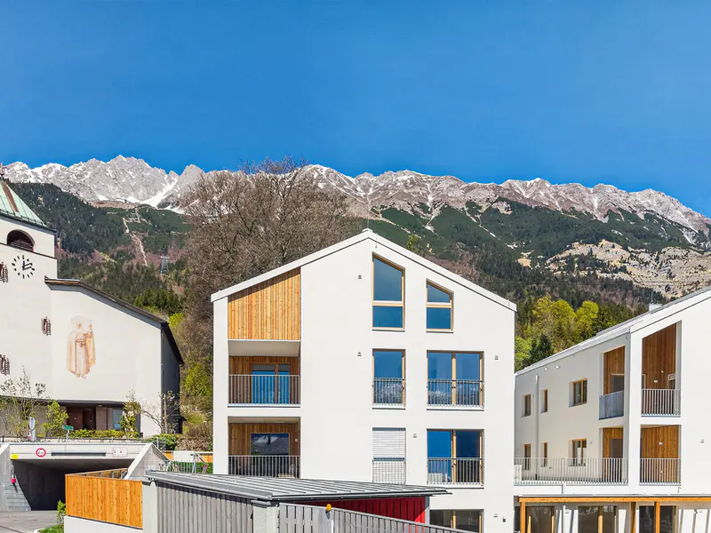 Modern white buildings with wood accents, balconies, and mountain views under a clear blue sky.