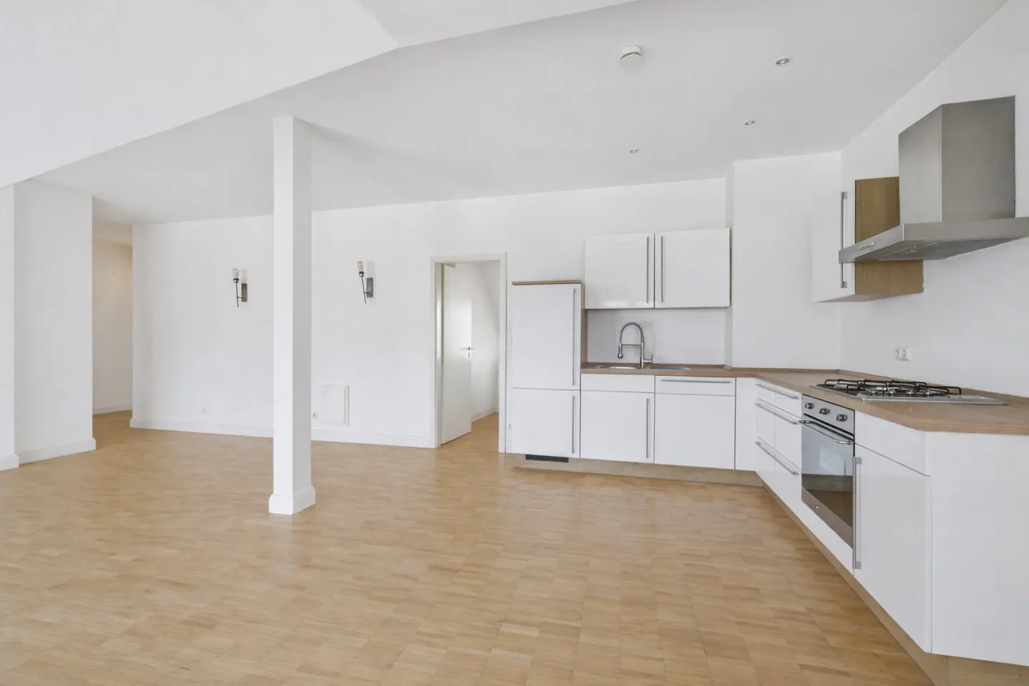 Bright, open-concept apartment with white walls, wood floors, and a modern white kitchen with stainless steel appliances.