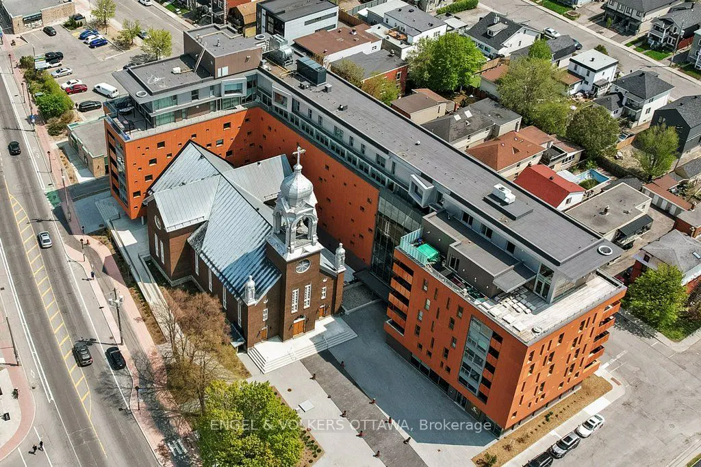 Aerial view of a historic brick church integrated with a modern orange and grey apartment complex in a city neighborhood.