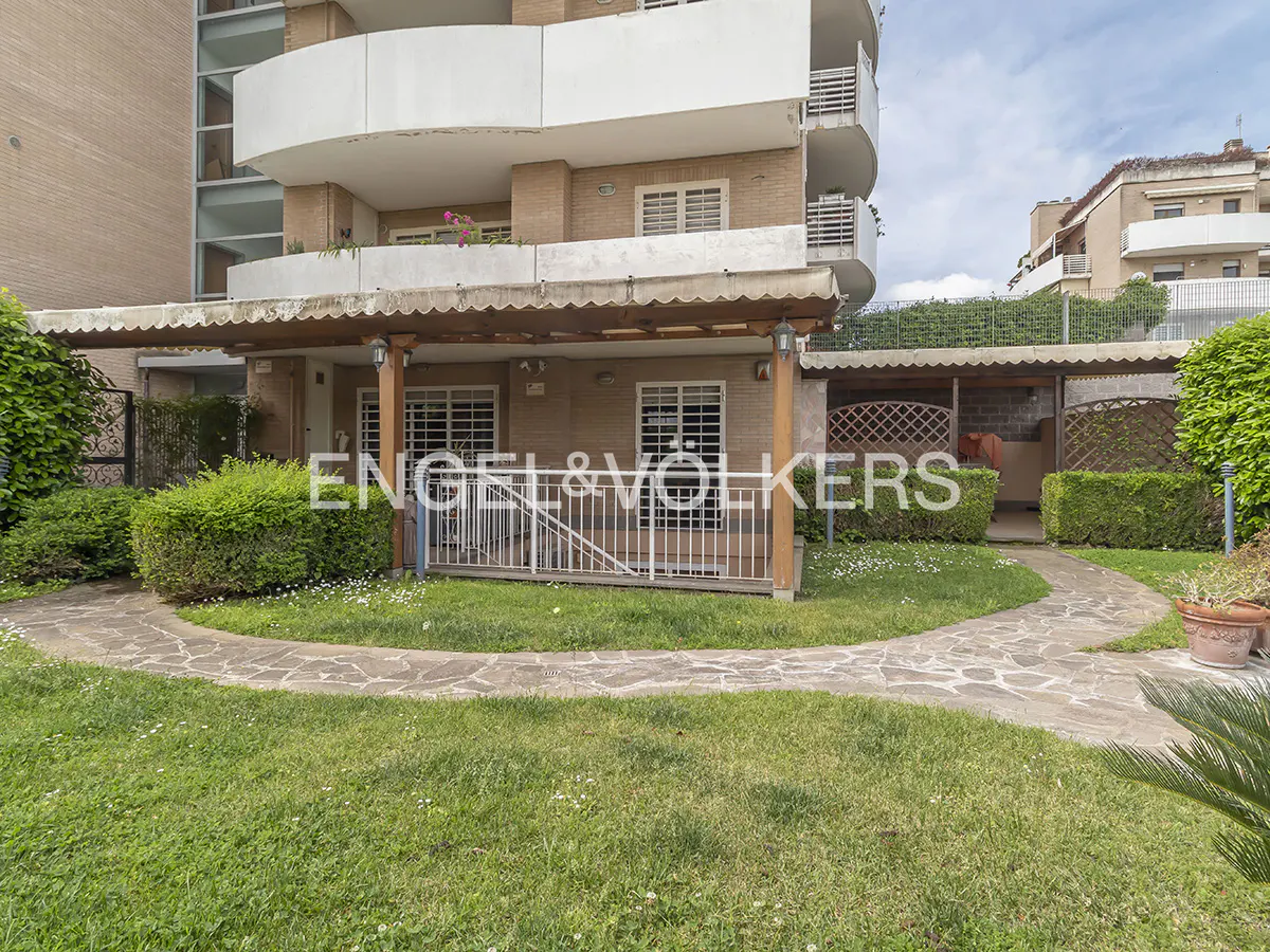 Exterior view of a tan apartment building with a stone walkway, green lawn, and Engel & Volkers logo.