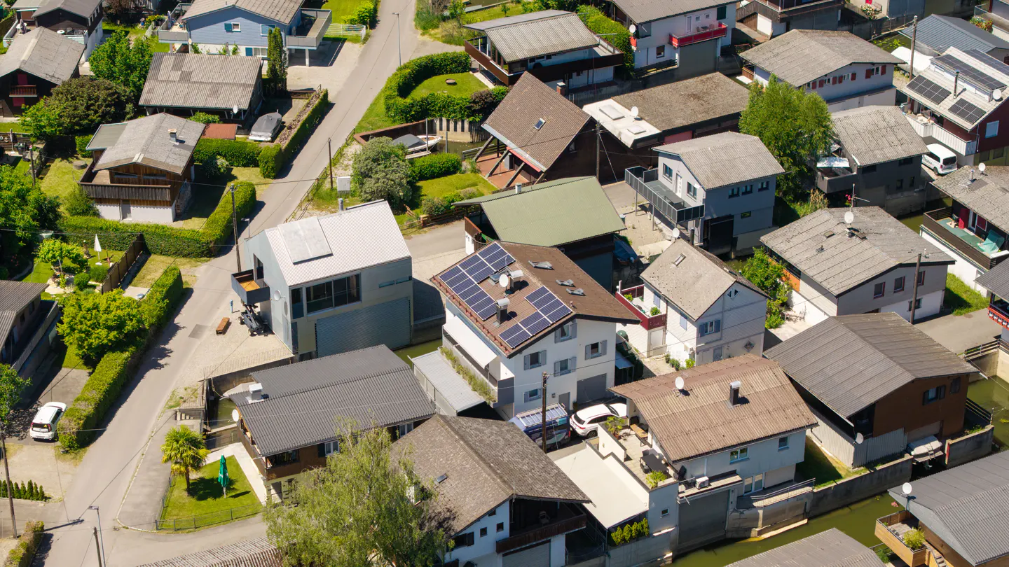 Aerial view of a dense residential neighborhood with various houses, pitched roofs, solar panels, and narrow streets.