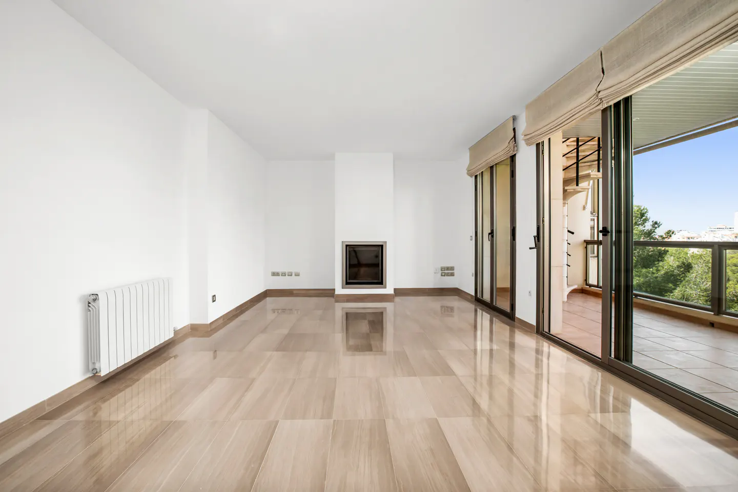 Bright, empty room with beige tile floor, white walls, and a fireplace. Sliding glass doors lead to a balcony with trees and a spiral staircase.