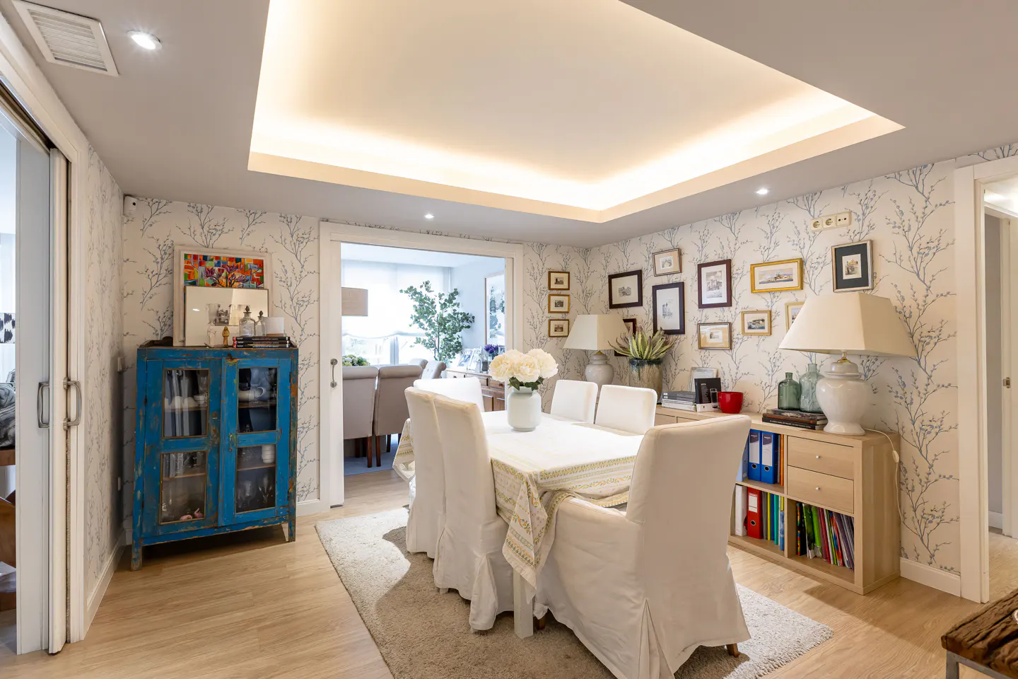 A dining room with a white table and chairs, a blue cabinet, and a gallery wall.