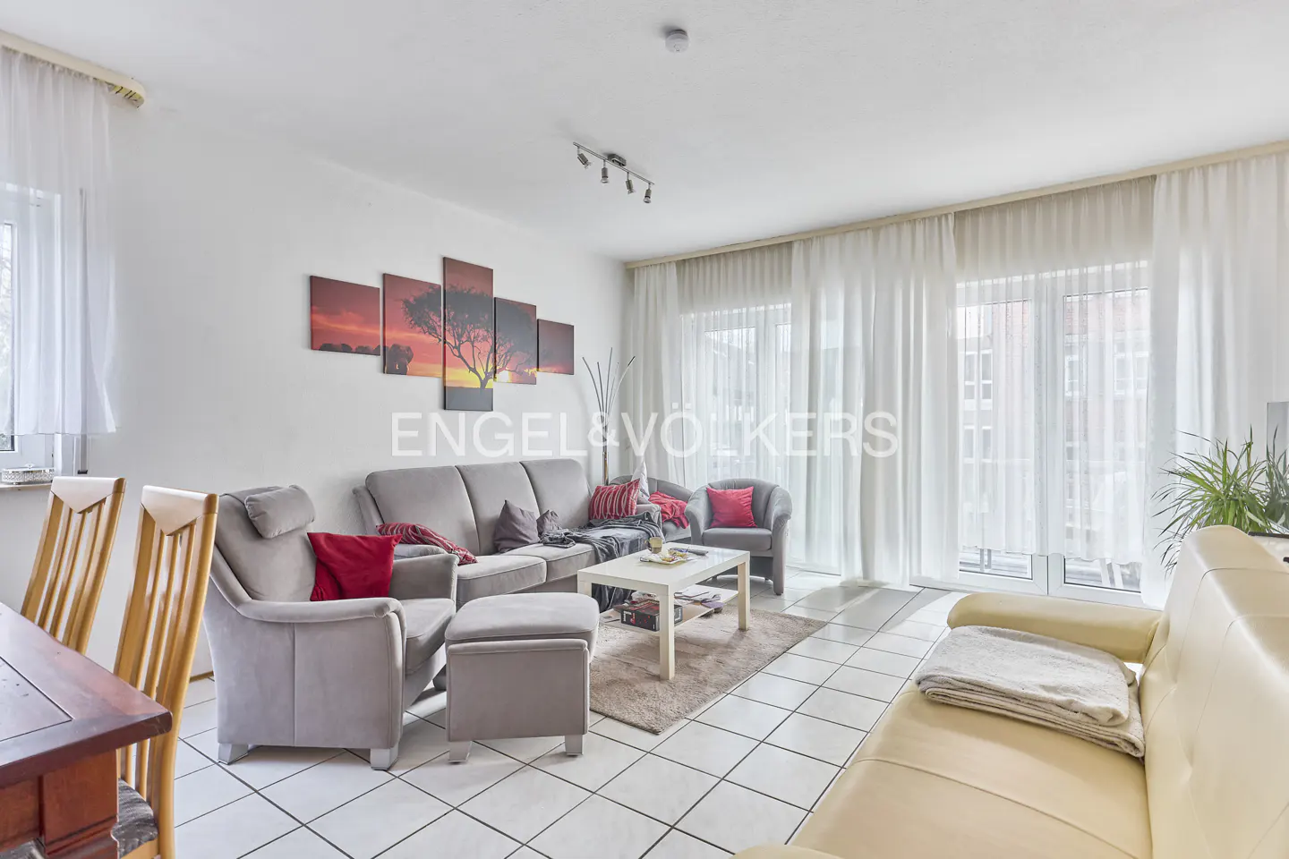 Living room with gray sofa, armchairs, white tile floor, and a sunset tree art piece on the wall.