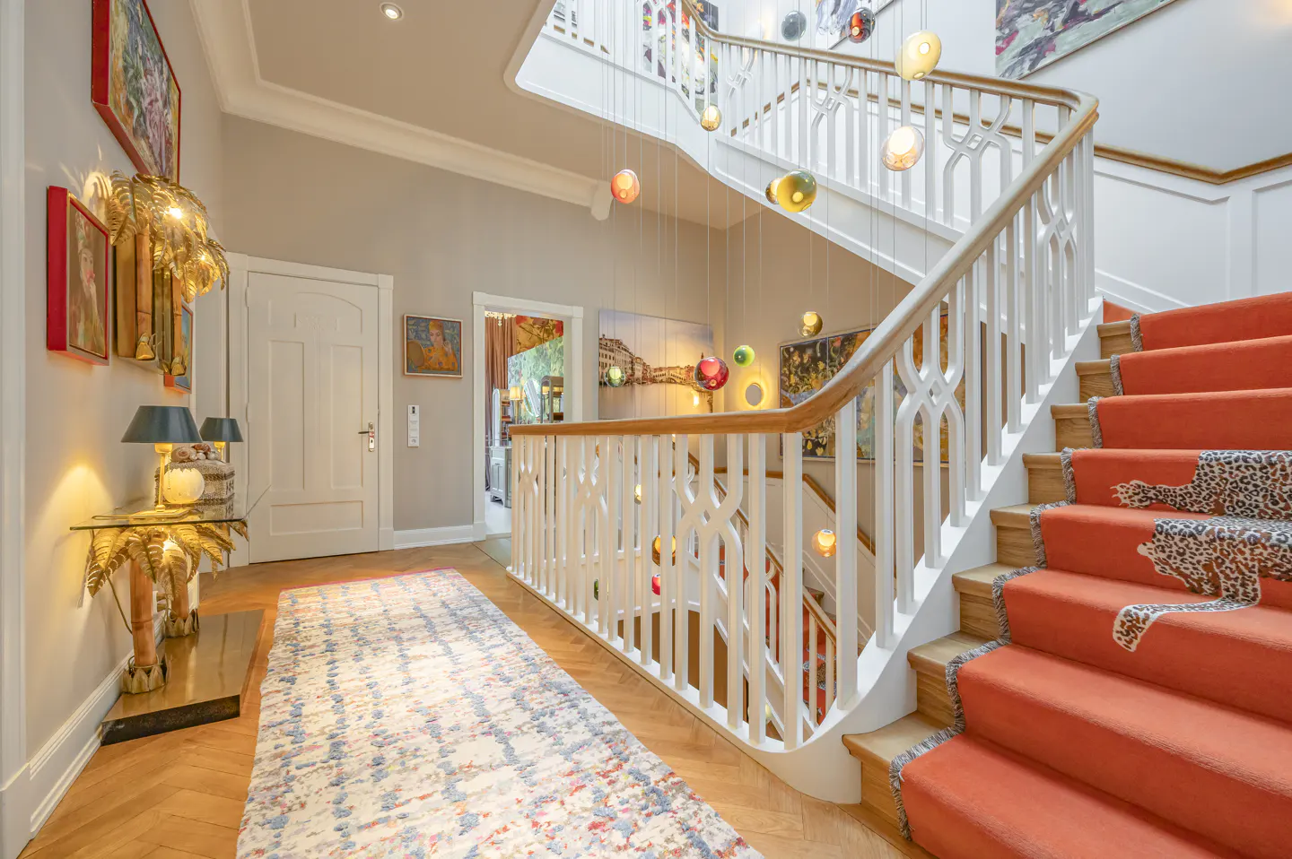 Grand foyer with a bright orange staircase featuring leopard-print runners, white railings, and colorful hanging lights.