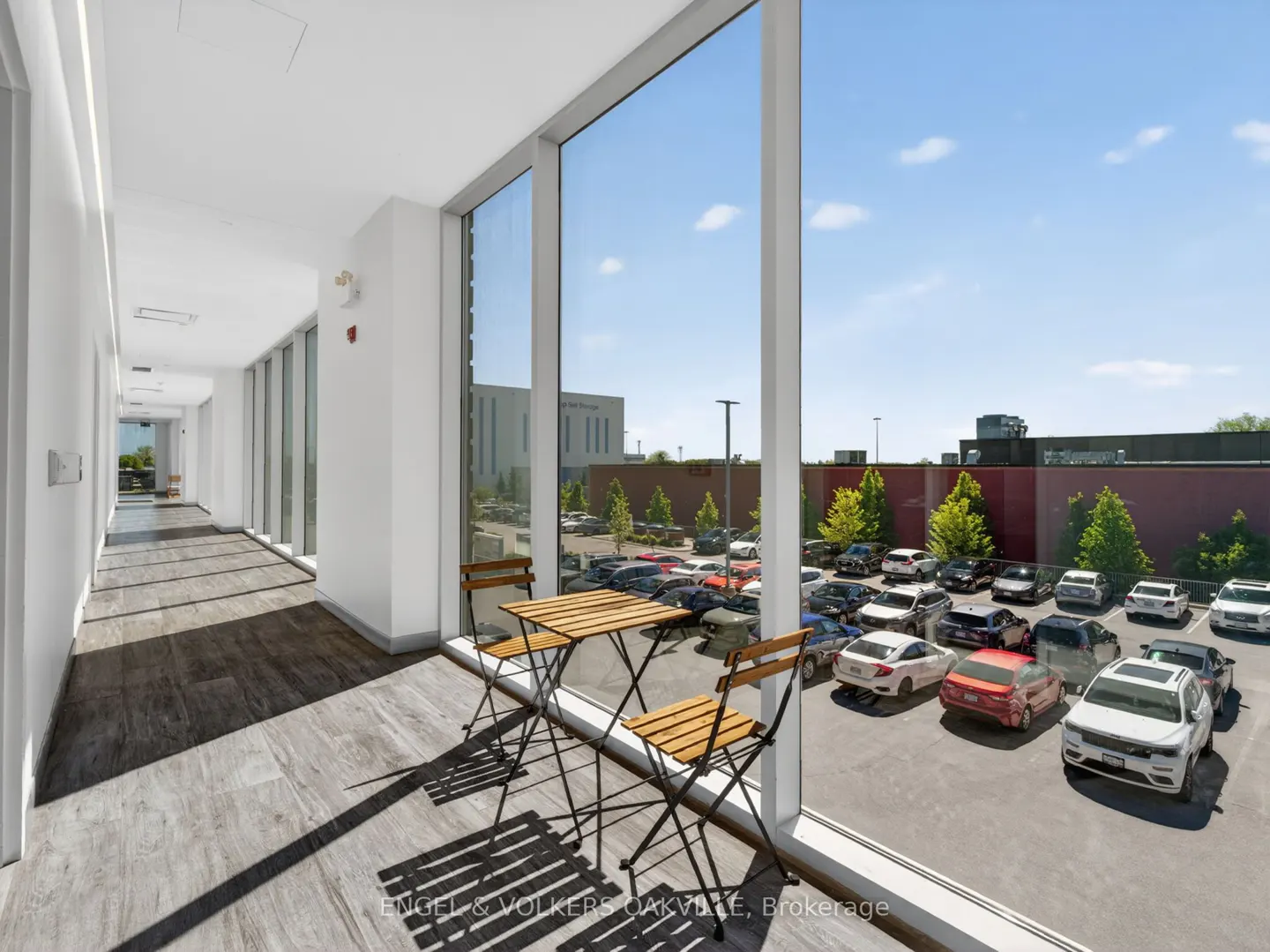 Hallway with wood-look tile and a table with two chairs overlooking a parking lot through a large window.