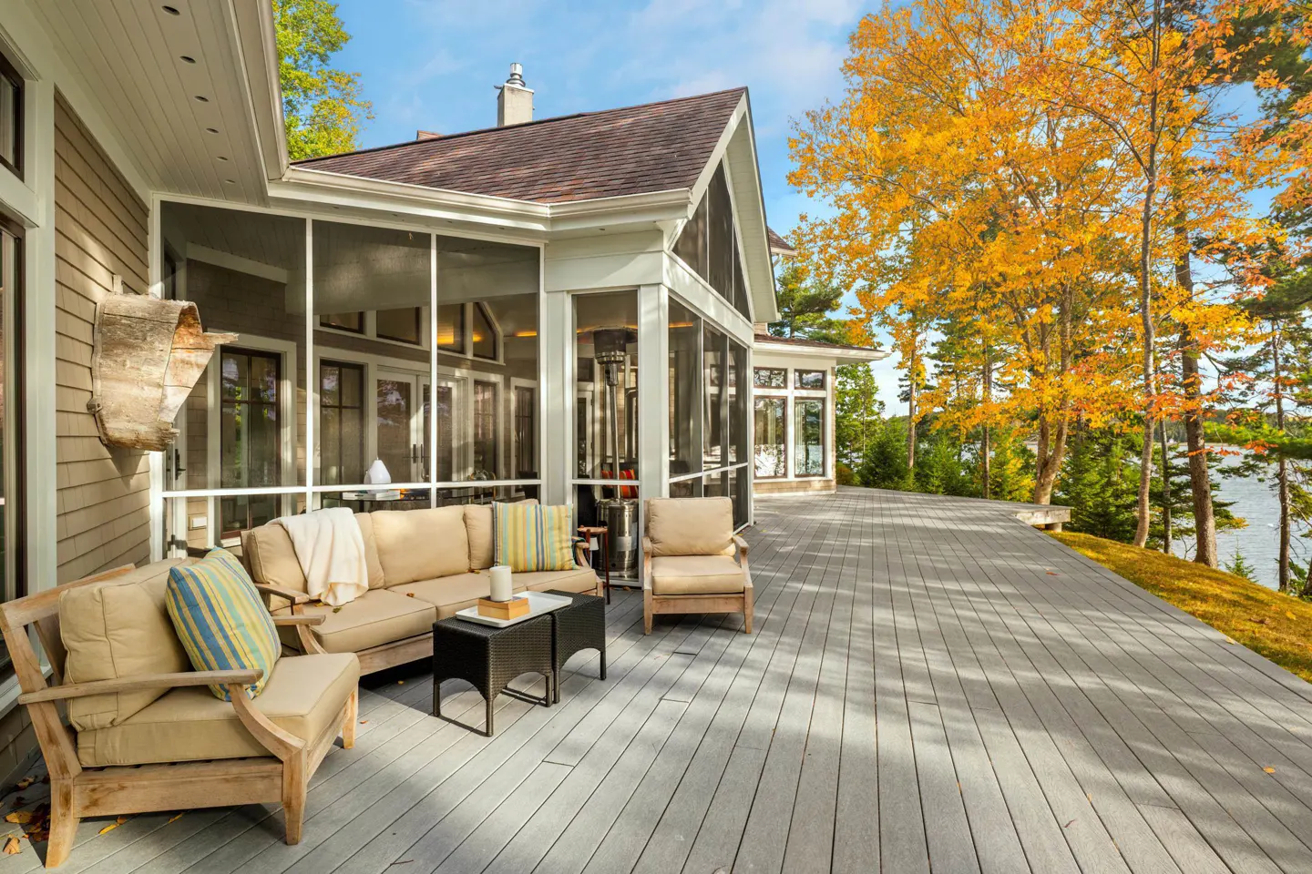 Outdoor patio with tan furniture on a gray deck, screened-in porch, and fall foliage.
