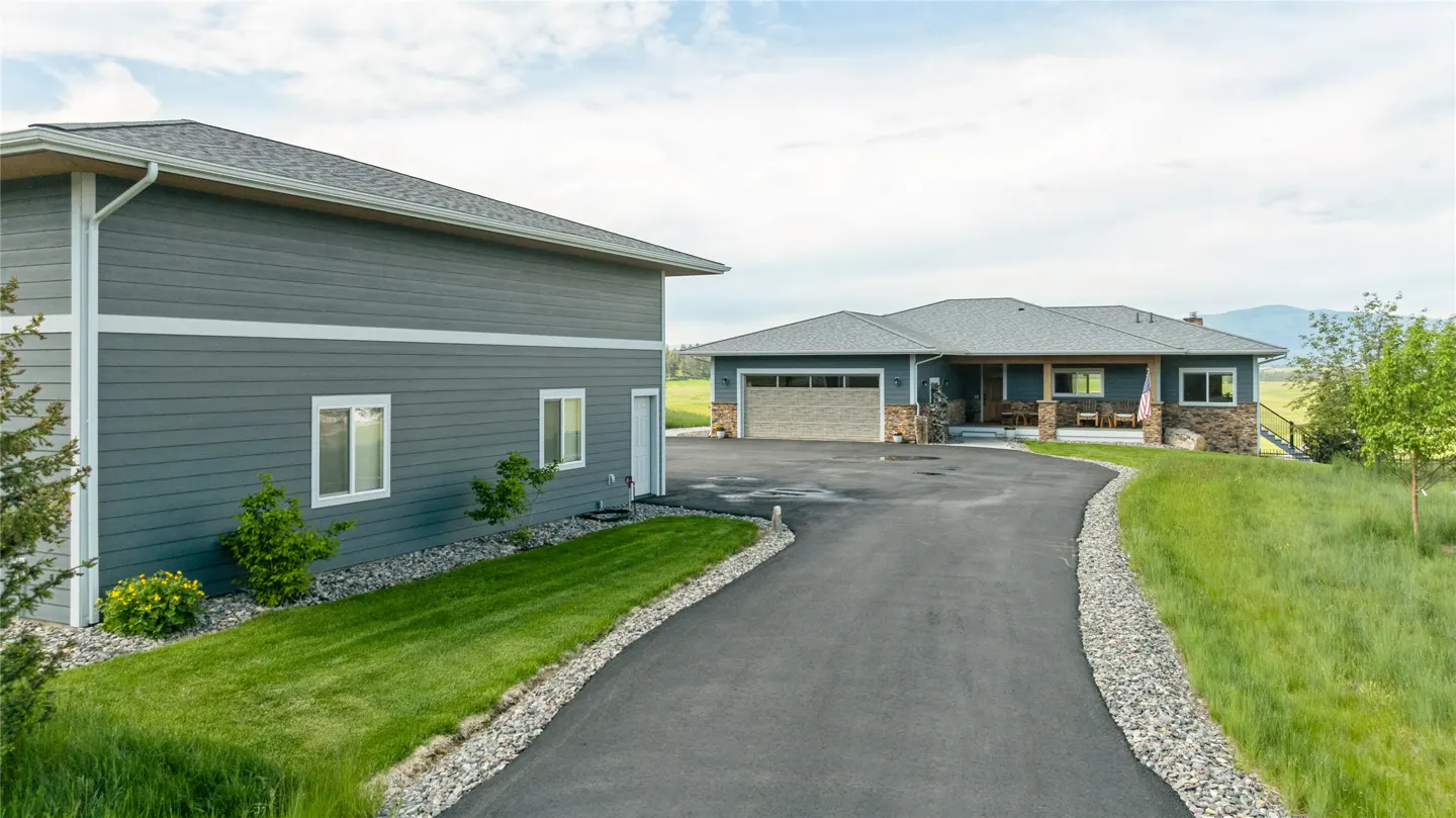 Exterior view of a gray house with a long driveway, green lawn, and a garage.
