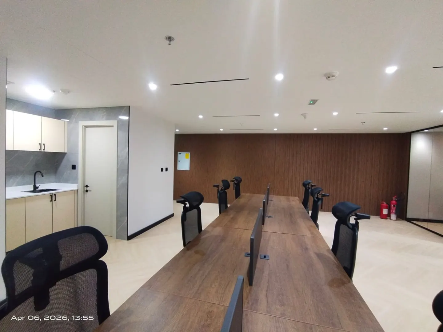 Bright office space with a long wooden table, black chairs, and a kitchenette in the corner.
