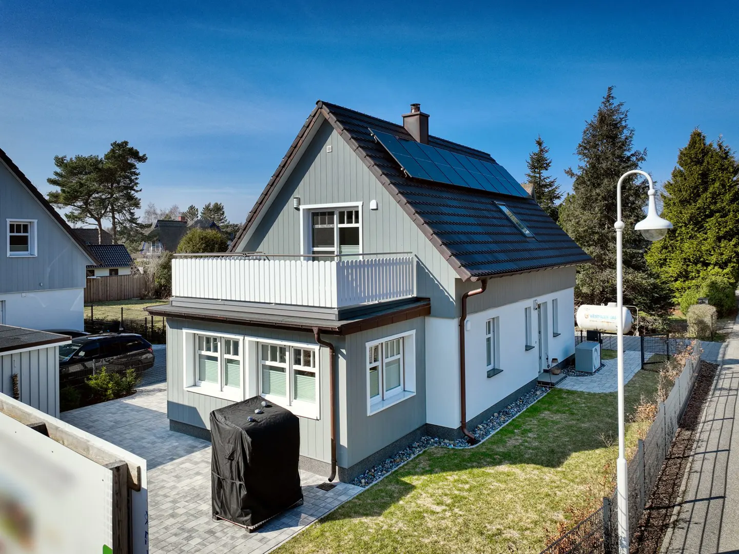 Two-story house with gray siding, white trim, and solar panels on the roof, viewed from above on a sunny day.
