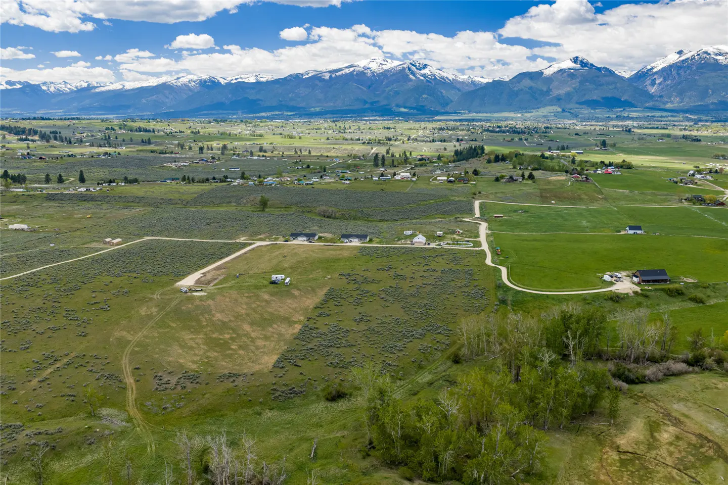 Aerial view of a green valley with snow-capped mountains in the background under a blue sky with white clouds.