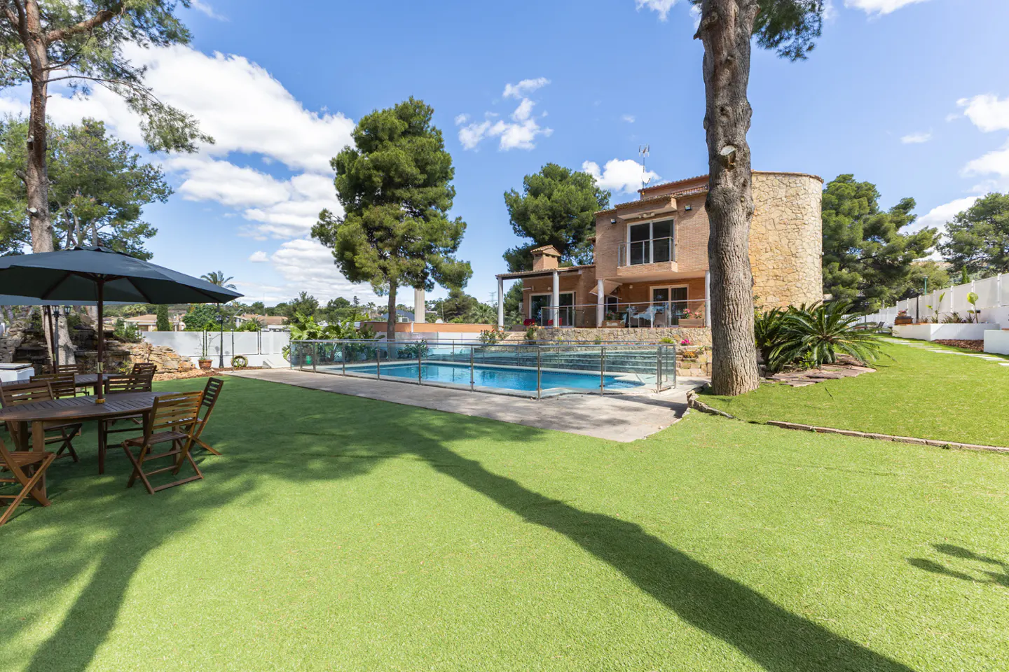 Exterior view of a tan house with a pool, green lawn, and patio furniture under a dark green umbrella.