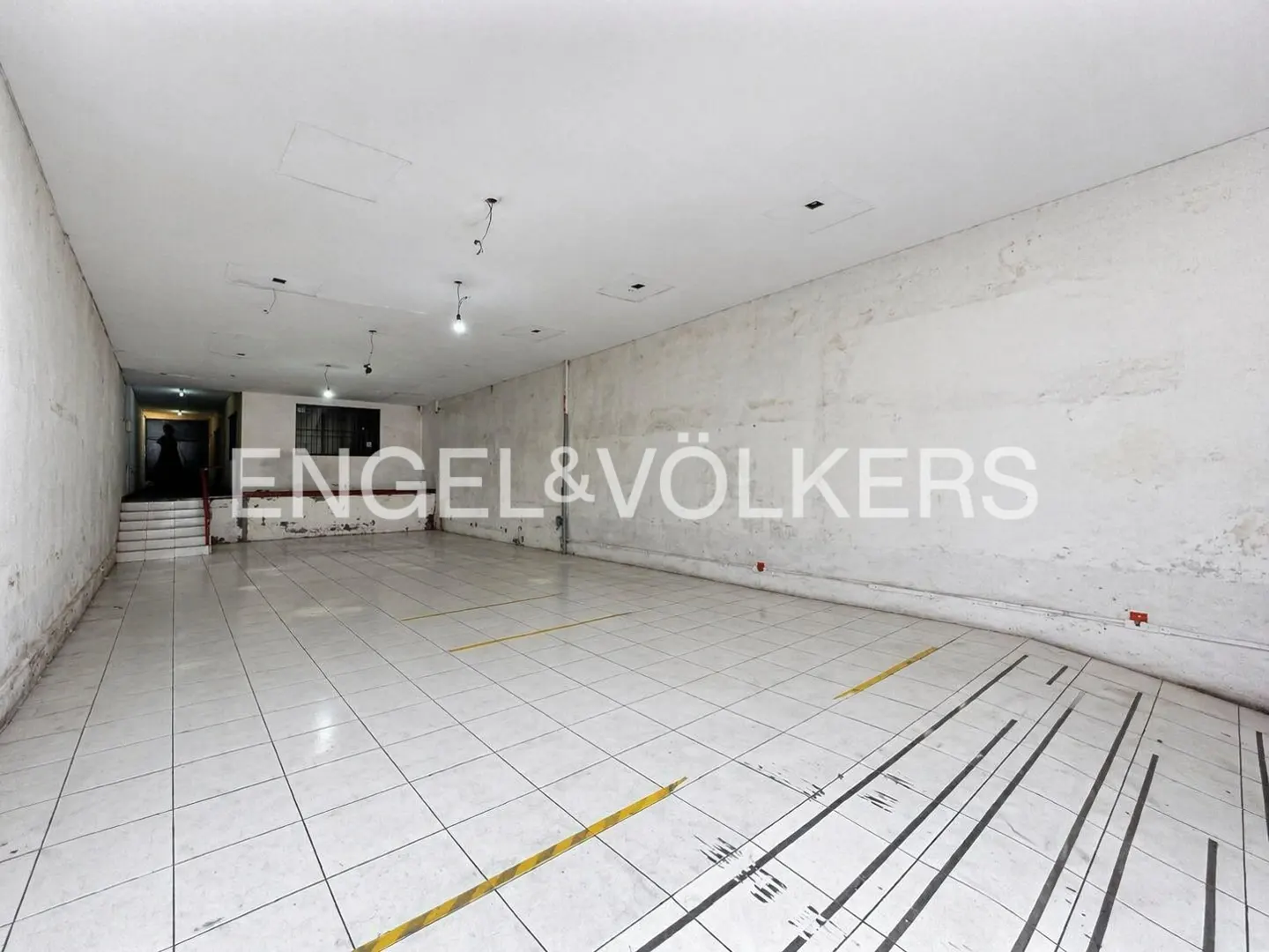 Empty commercial space with white tile floor, peeling white walls, and Engel & Völkers logo.