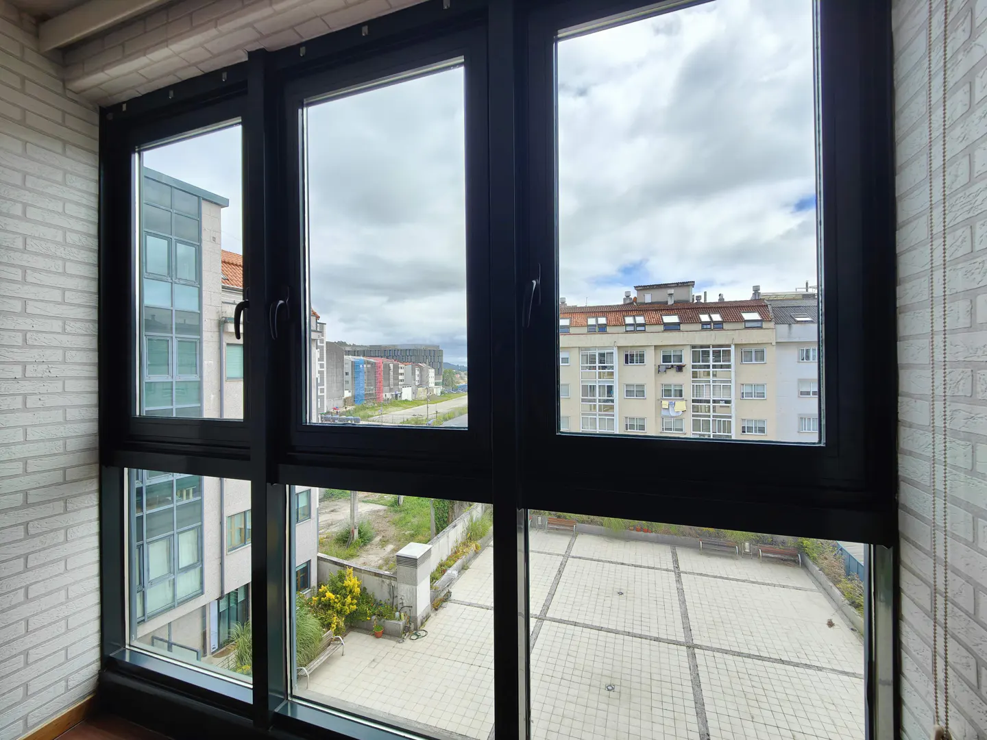 View from a window showing a paved courtyard, surrounding apartment buildings, and a cloudy sky.