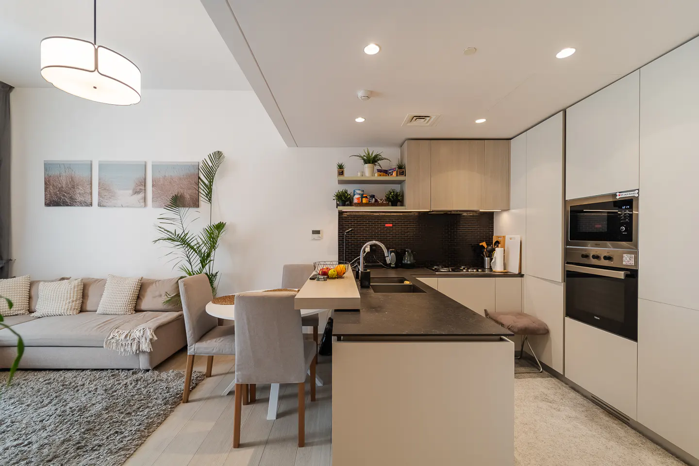 A modern kitchen and living room area with a gray sofa, round table, and island with a dark countertop.